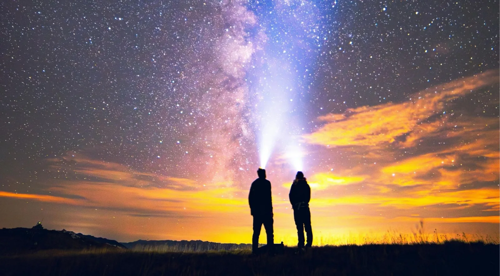 Two people wearing head torches beneath the Milky Way as the last orange light leaves the sky