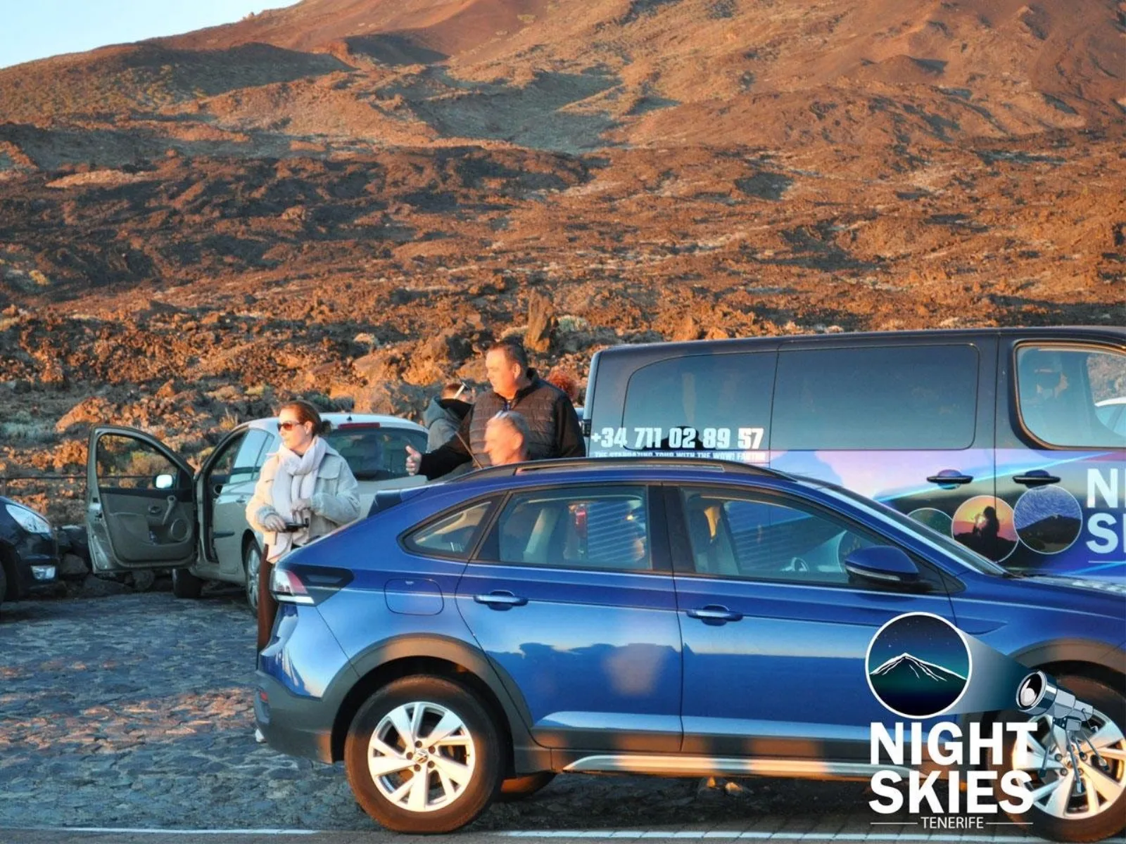 Guests beside the operator's blue minivan on the caldera floor at sunset
