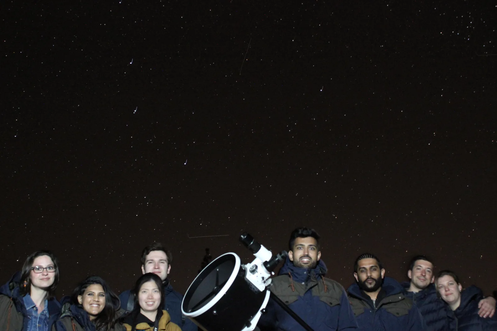 A tour group standing behind a large white Dobsonian telescope under the stars