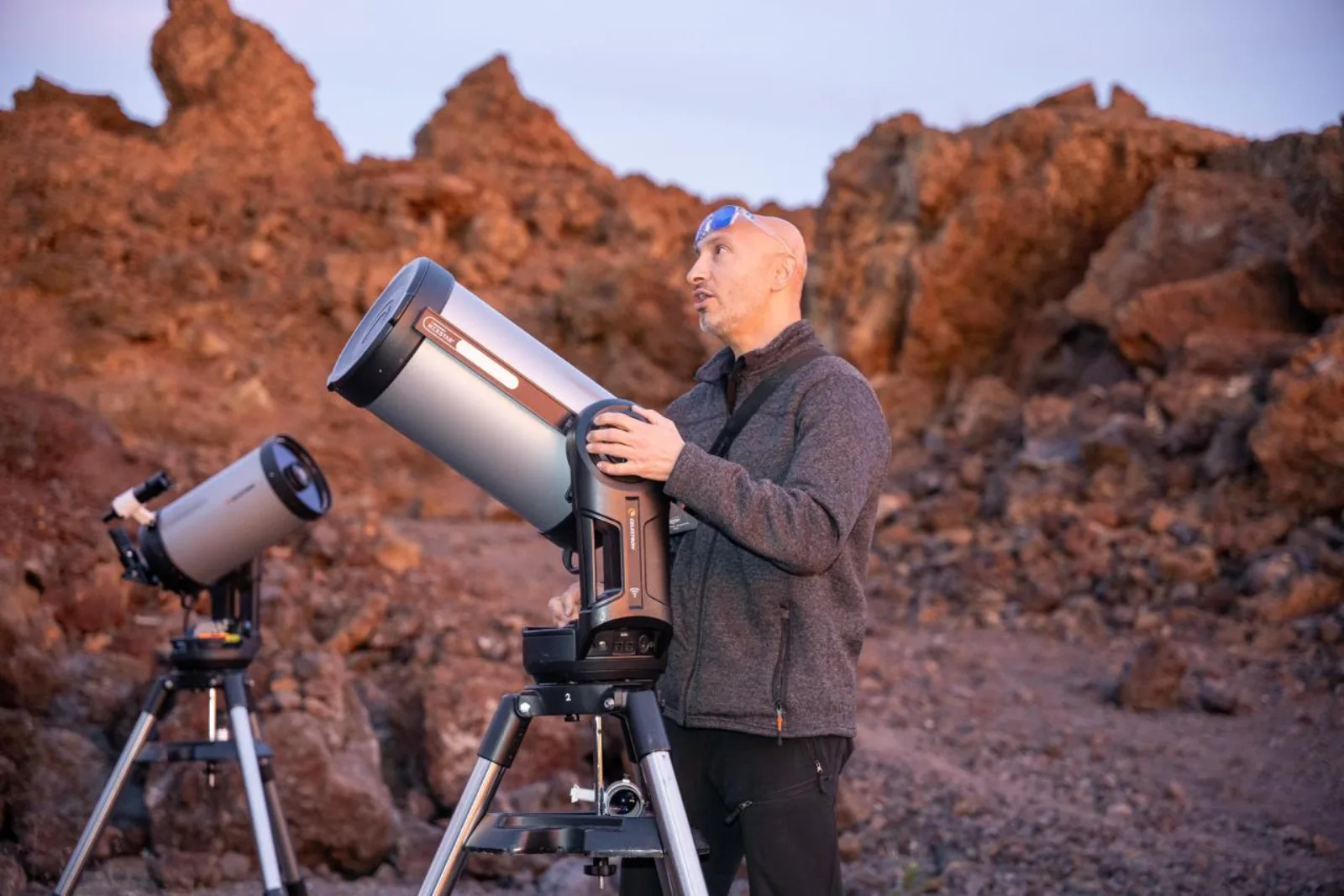 A guide setting up a Schmidt-Cassegrain telescope on red volcanic ground at dusk