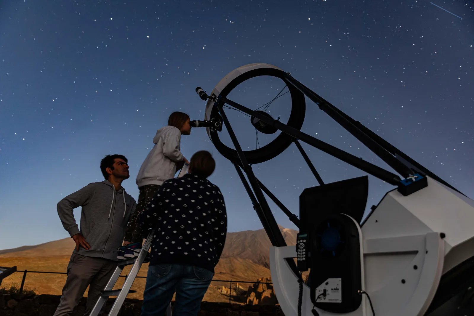 Two visitors at the eyepiece of the giant Dobsonian against deep blue twilight