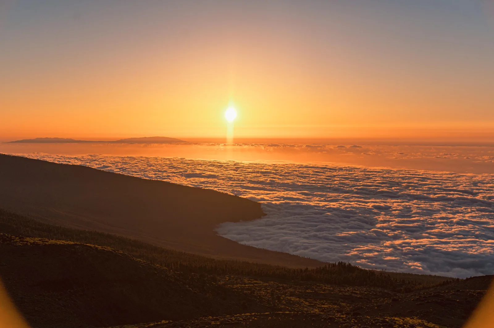 The sun setting into a sea of clouds seen from the caldera rim
