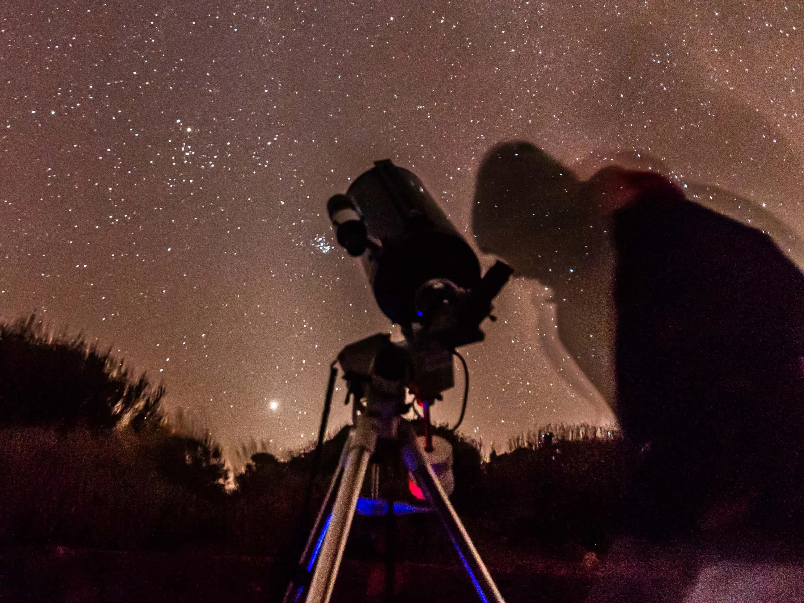 An 8-inch telescope on its tripod under the stars beside a rock outcrop