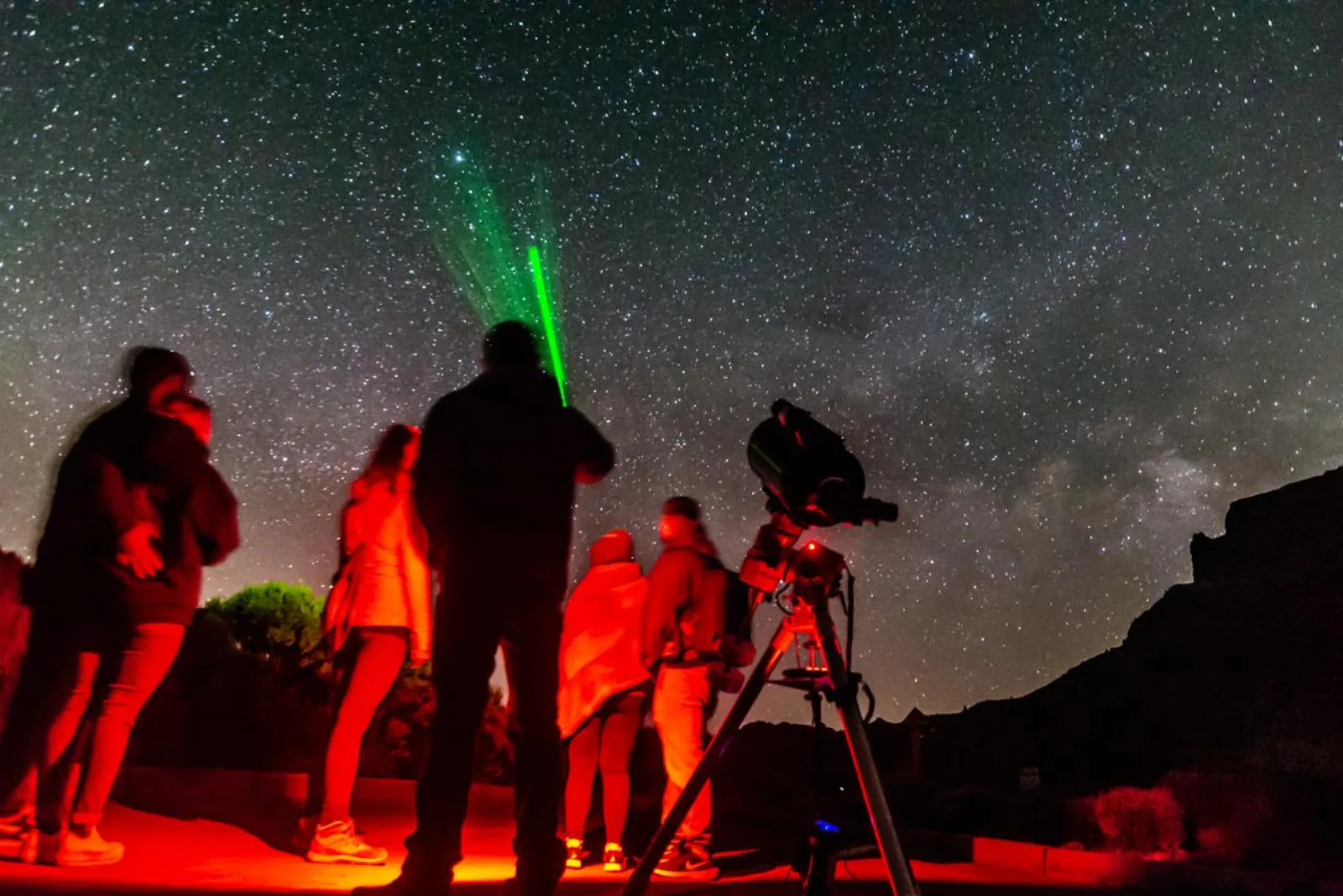The group under red light as the guide's green laser marks a target between two telescopes