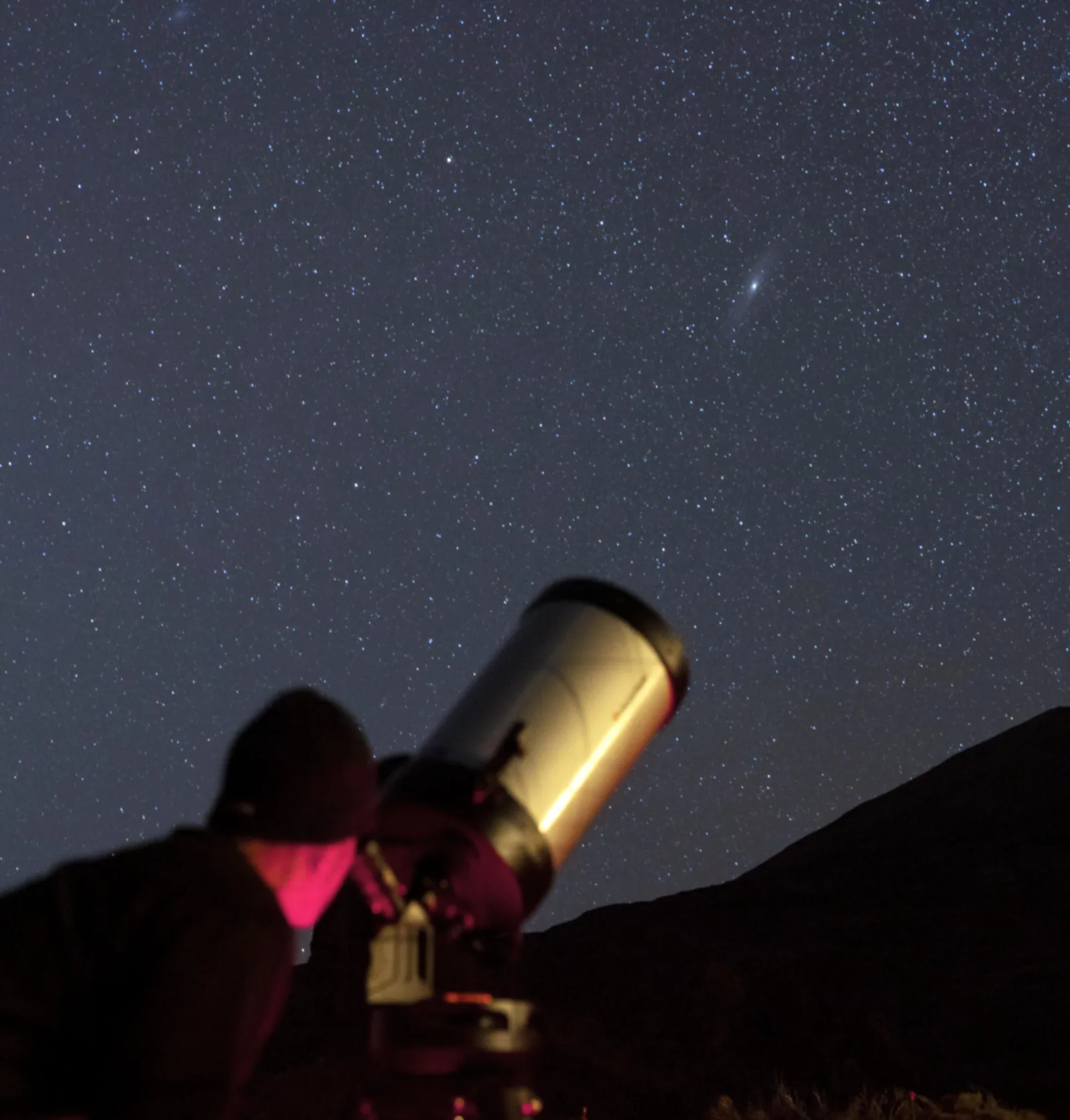 A telescope tube aimed at the Andromeda galaxy, visible as a faint smudge above