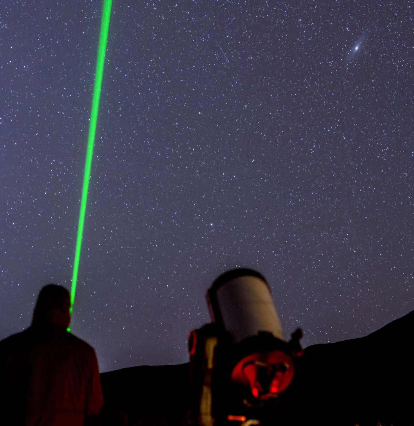 A green laser beam pointing into the star field beside the telescope