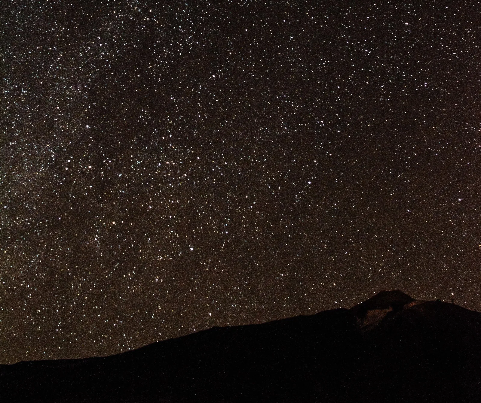 A dense field of stars above a low mountain silhouette